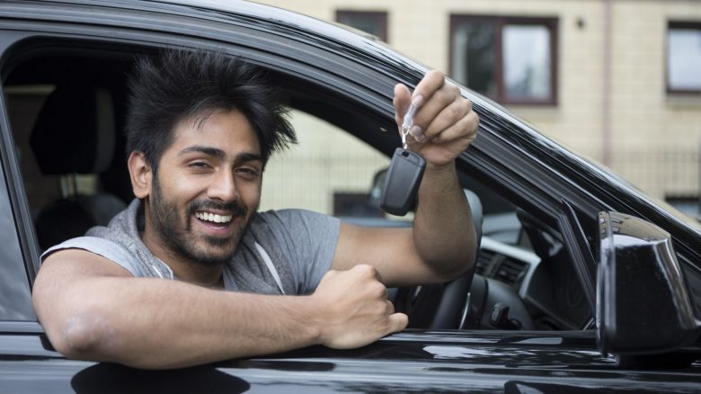 Young driver leaning out of car with keys in hand