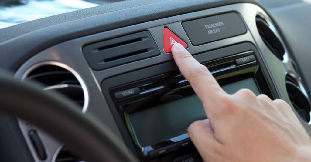 Person's finger resting on the hazard warning lights button on the car dashboard