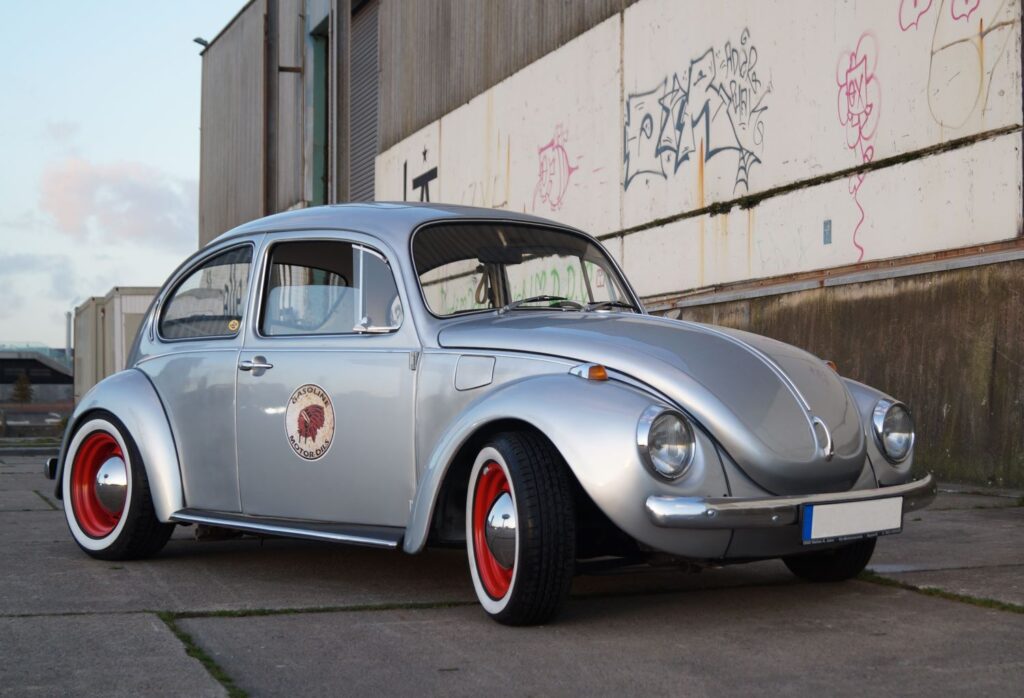 Grey modified VW Beetle parked outside a building with graffiti on it
